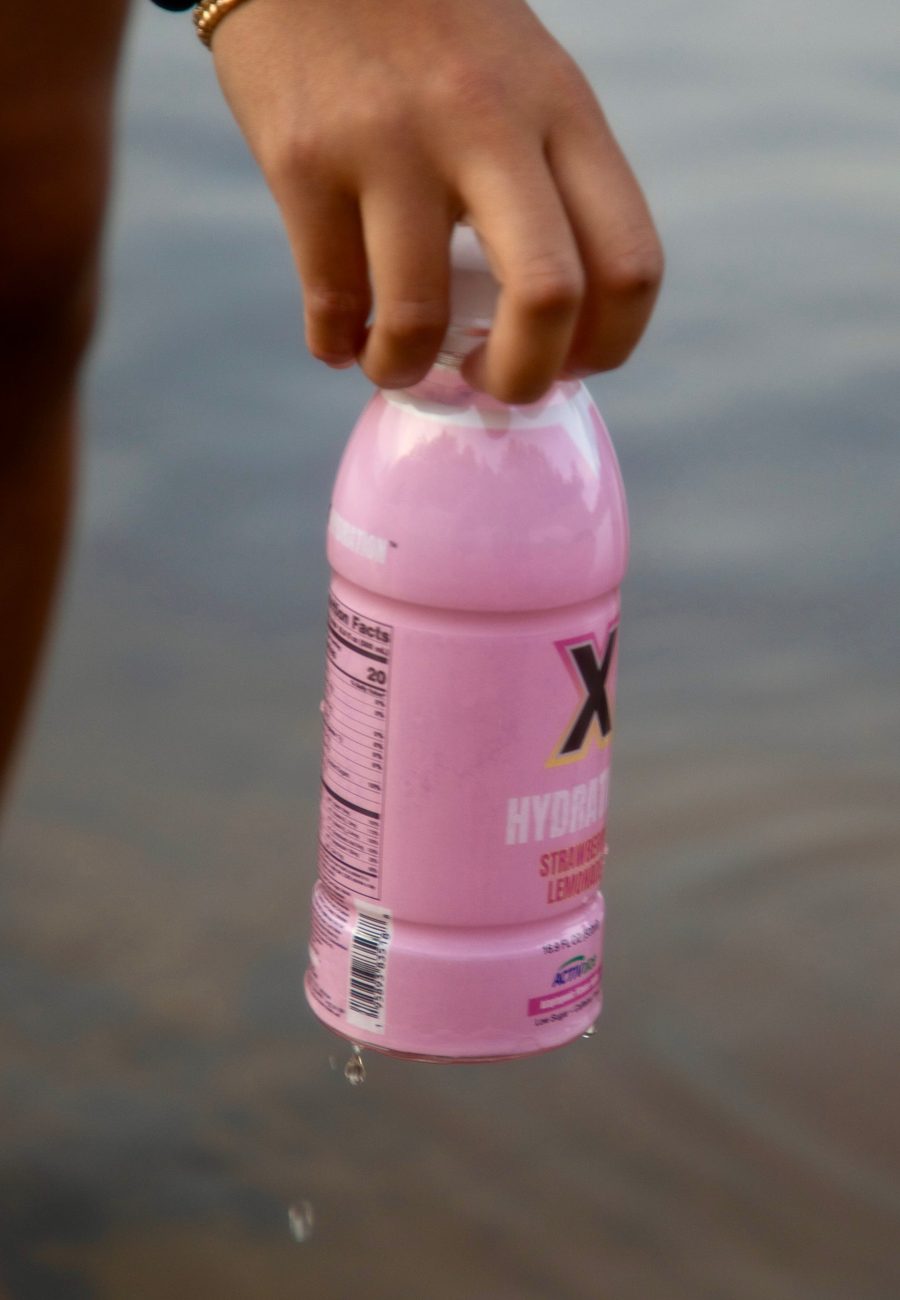 Hand holding a bottle of X Hydration Strawberry Lemonade over the water